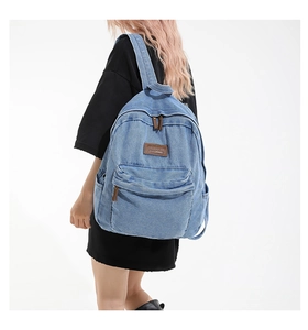 Detail view of light blue denim backpack with front pocket and brown leather logo patch
