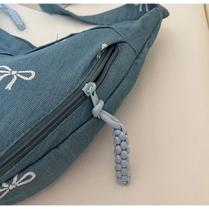 Detail der blauen Jeans-Umhängetasche mit weißem Schleifendruck und Web-Reißverschluss