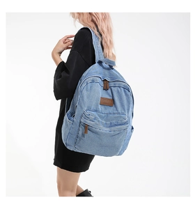 Detail view of denim backpack showing brown leather logo and vintage washed texture fabric