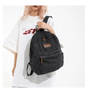 Detail of black denim backpack featuring leather logo patch and front zipper pocket