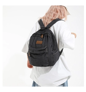 Detail of grey denim backpack featuring brown leather logo patch on a model back