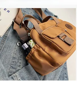 Detail of a brown nylon crossbody bag with multiple pockets on a denim jacket