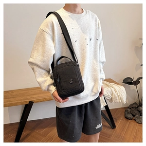 Detail of a black nylon crossbody bag with multiple zippers and adjustable strap