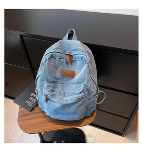 Close-up of light blue denim backpack with brown leather logo patch and zipper puller