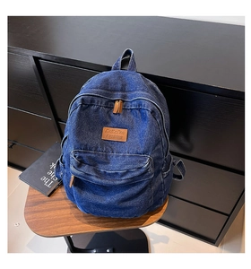 Detailed close-up of blue denim backpack with brown leather patch and zip puller accent