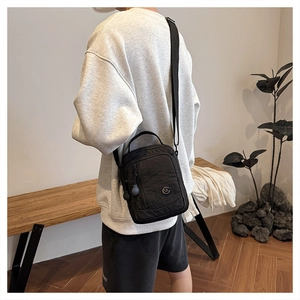 Detail of a lightweight black nylon crossbody bag with adjustable strap and front zipper