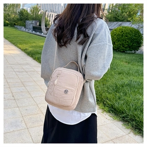 Outdoor shot of a beige nylon crossbody bag with textured fabric and metal logo