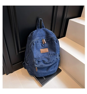 Detailed close-up of dark denim backpack texture with leather logo and bronze zippers