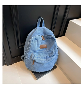 Close-up of light blue denim backpack showing the leather label and twill fabric detail