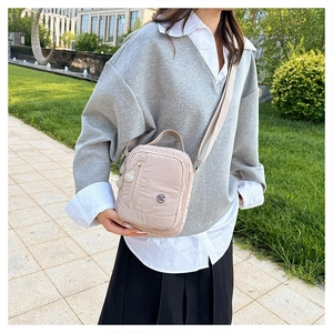 Detail view of water-resistant beige nylon crossbody bag with front zipper and metal logo