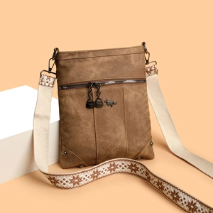 Brown canvas crossbody bag with bohemian patterned wide strap on a studio prop