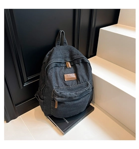 Detailed macro view of black denim backpack with leather logo patch and brown zipper puller