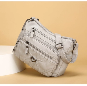 Détail du sac bandoulière beige avec plusieurs zips et décoration métallique en cœur