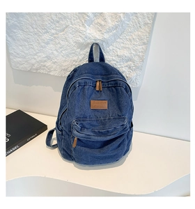 Detail of blue denim backpack showing front zipper pocket and brown leather logo patch