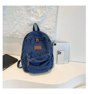 Detailed view of dark blue denim backpack with fashion leather patch and front pocket