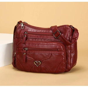 Détail du sac bandoulière en cuir rouge foncé avec multi-poches et boucle cœur en métal