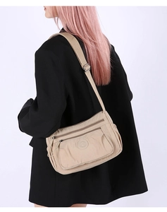 Beige multi-pocket nylon crossbody bag worn on black blazer showing tiered zip layers