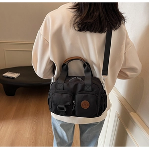 Detail of a black multi-pocket canvas crossbody bag with brown leather handles and side pleats