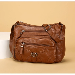 Détail d'un sac bandoulière marron en cuir souple avec poches zippées et breloque cœur