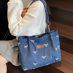 Blue denim tote bag with white bow pattern and chain straps shown on person's shoulder