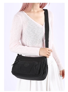 Close-up of black nylon multi-pocket crossbody bag with adjustable wide strap on model