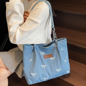 Blue denim tote bag with white bow pattern and chain strap shown on a model