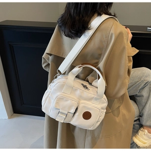 Detail of white canvas crossbody bag with multi-pocket design and brown leather logo patch