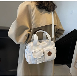 Detail of white canvas crossbody bag showing dual front pockets and adjustable shoulder strap