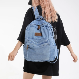 Large light blue denim backpack with leather details shown on a model against white background