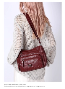Détail d'un grand sac bandoulière bordeaux en similicuir avec plusieurs zips et boucle cœur