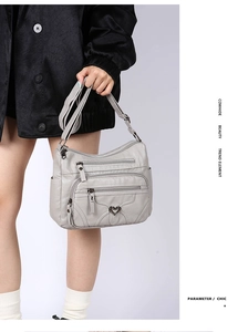 Détail du sac bandoulière en cuir souple gris avec triple zip et accents en métal cœur