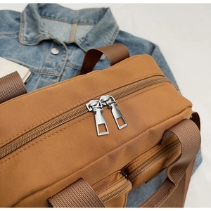 Close-up of the durable dual metal zippers on a brown water-resistant nylon crossbody bag
