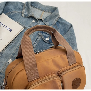 Close-up of brown waterproof nylon crossbody bag with dual front zipper pockets and strap