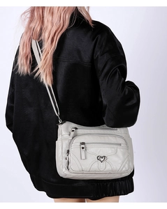 Détail du sac bandoulière en cuir synthétique souple avec poches zippées et breloque cœur