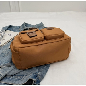 Detailed view of camel brown fabric bag with two front pockets and logo patch on denim