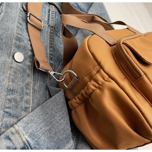 Detail of khaki water-resistant nylon crossbody bag with metallic hardware on denim jacket