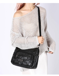 Détail d'un sac bandoulière noir en similicuir avec plusieurs fermetures éclair et boucle cœur