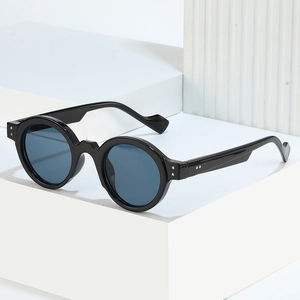 Retro round frame sunglasses with black frame, blue lenses and silver rivets on white podium