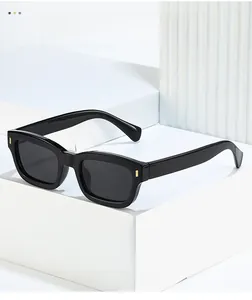 Detail of black square sunglasses with gold hinge accents on a white geometric stand