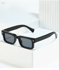 Detail of black square sunglasses with gold metal studs on a white geometric stand