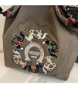 Dettaglio del ricamo colorato con cavalli e logo a ferro di cavallo su borsa marrone