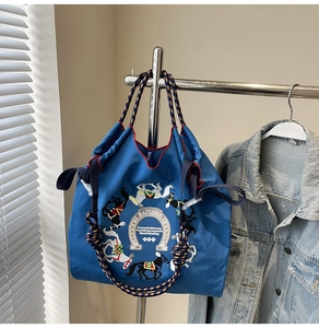 Dettaglio del ricamo a cavallo e della borsa tote blu con manici in corda intrecciata