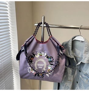 Dettaglio della borsa tote viola in tessuto oxford con ricamo cavallo e manici intrecciati