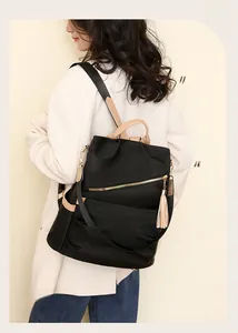 Detail of black nylon backpack with beige leather trim and tassels worn over a white coat
