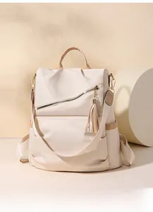 Detail of beige nylon backpack featuring diagonal zipper, leather trim and tassel charm