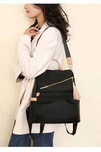 Detail of black nylon backpack with brown leather trim and tassel on a female model