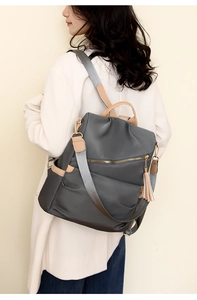Close-up of grey nylon backpack with brown leather trim and tassel on a female model