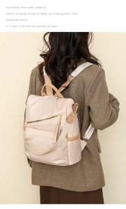 Detail view of beige nylon backpack featuring gold zippers and decorative tassel charm