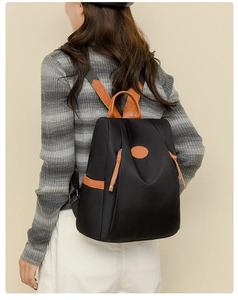 Detail view of anti-theft oxford backpack with brown leather trim on striped knit sweater