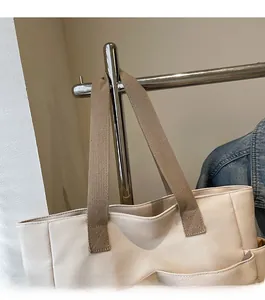 Close-up of wide canvas shoulder strap and reinforced stitching on off-white tote bag